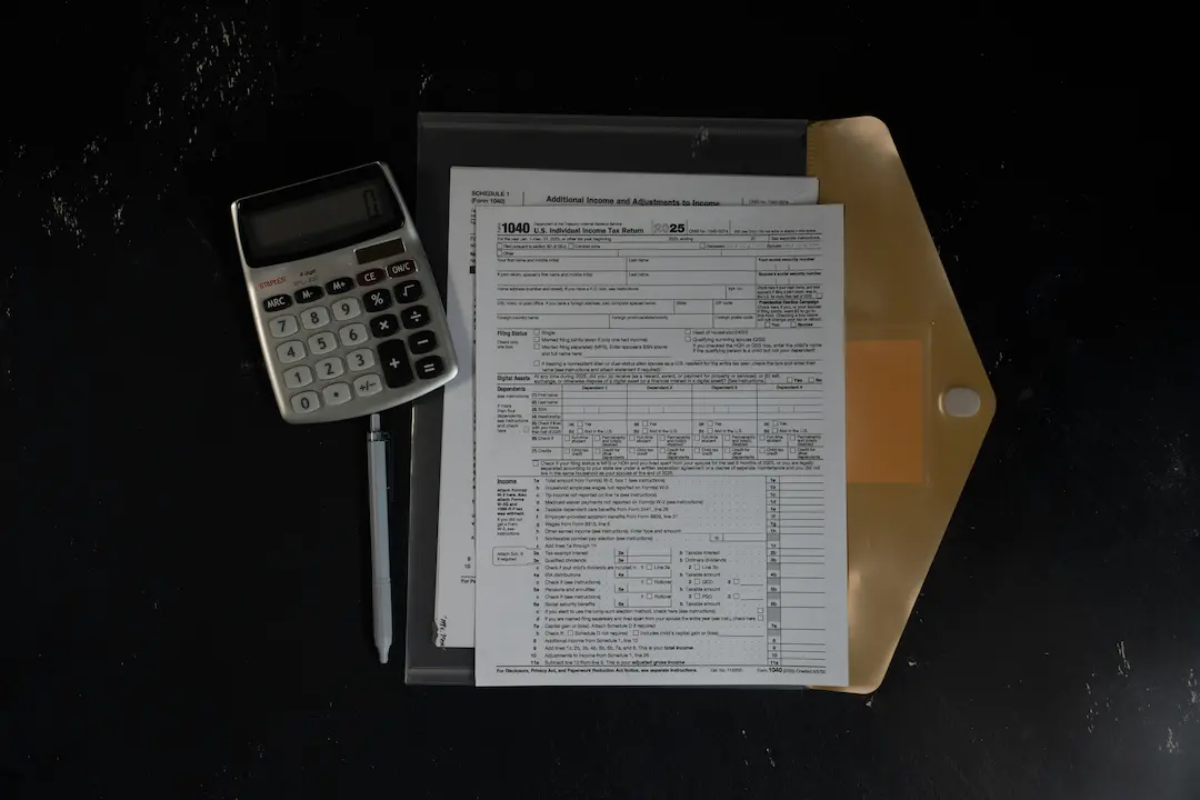 Widok z góry na kalkulator, długopis i szczegółowe dokumenty w teczce na czarnym tle, sugerujący pracę biurową lub finansową.
